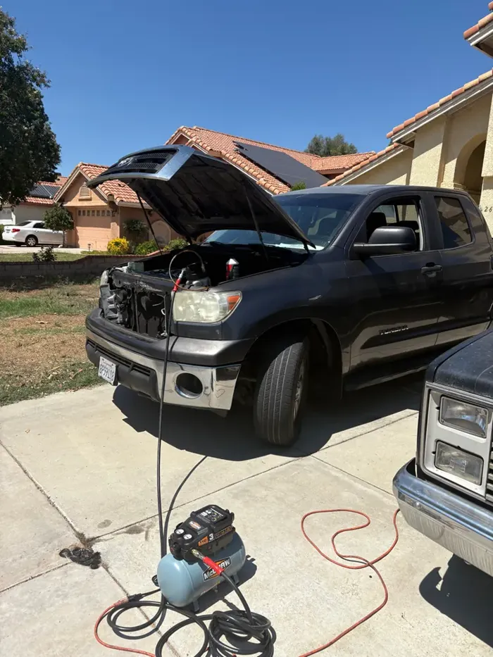 A Tundra in the driveway, hood up, charger on